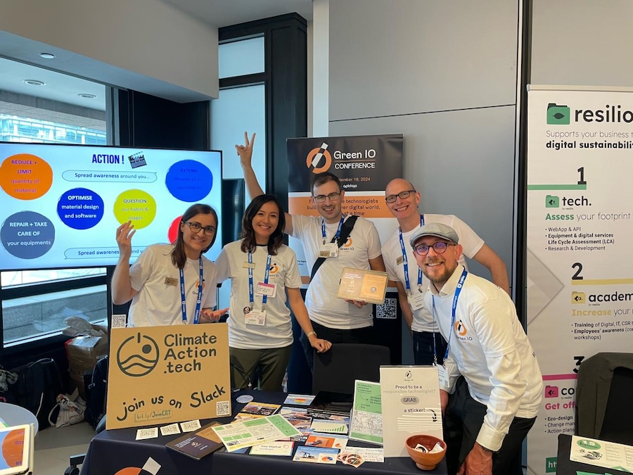 Five people around a conference table full of promotional material. They are all wearing Green IO shirts, and smiling at the camera